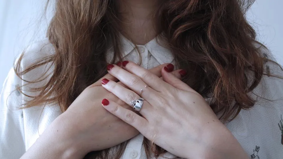 Hands with glossy dark red nail polish resting on a white blouse