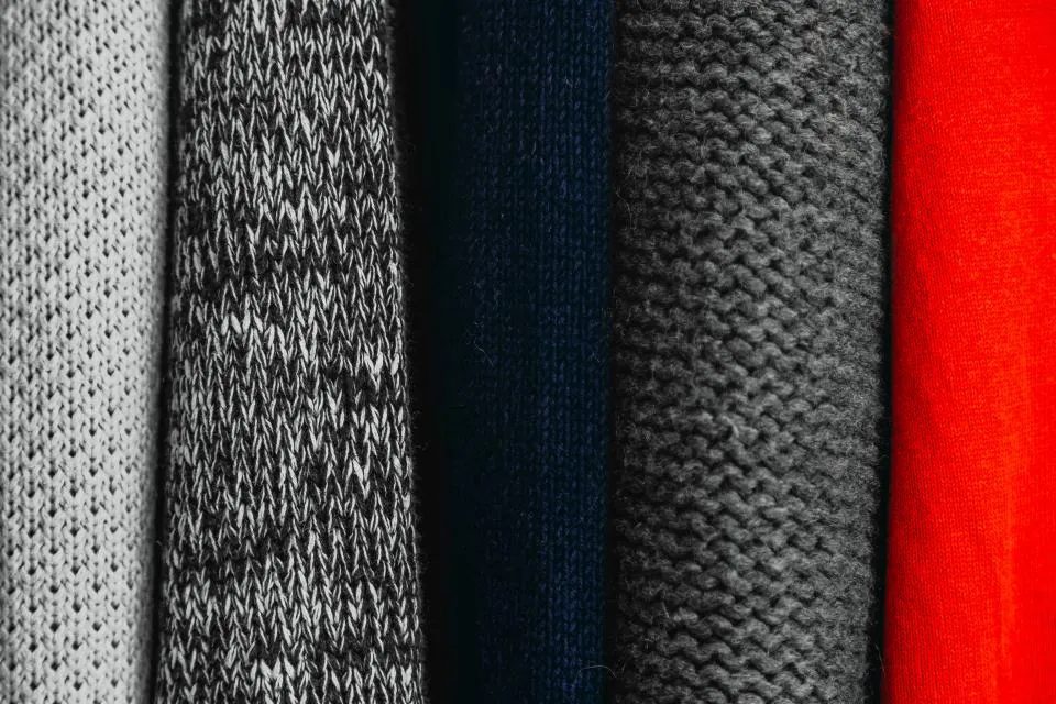 Stack of knit sweaters in gray, navy and red fabrics that may need nail polish stain removal