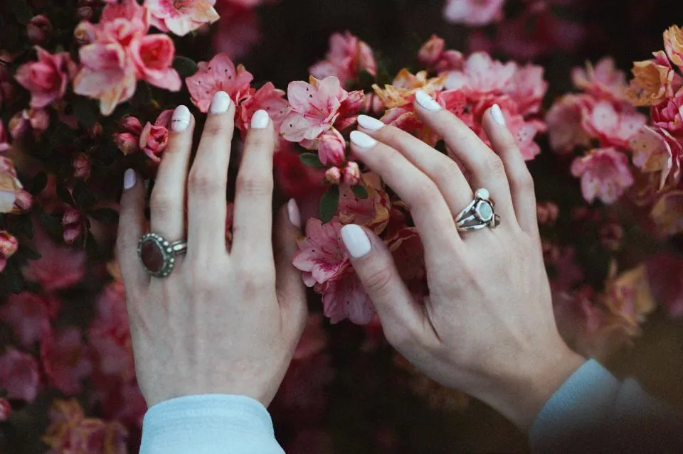 Hands with glossy white gel nails finished with a no wipe top coat, resting on pink flowers