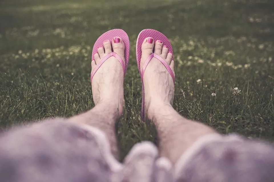 Feet with pink pedicured toenails in pink flip flops on green grass