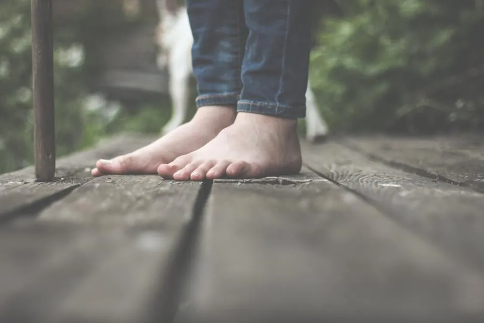 Bare feet standing on a wooden deck, a reminder of how to get rid of calluses on feet with gentle care