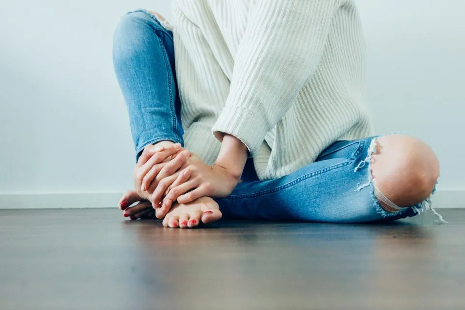 Woman sitting on the floor with freshly painted red toenails, showing how to make a pedicure last longer