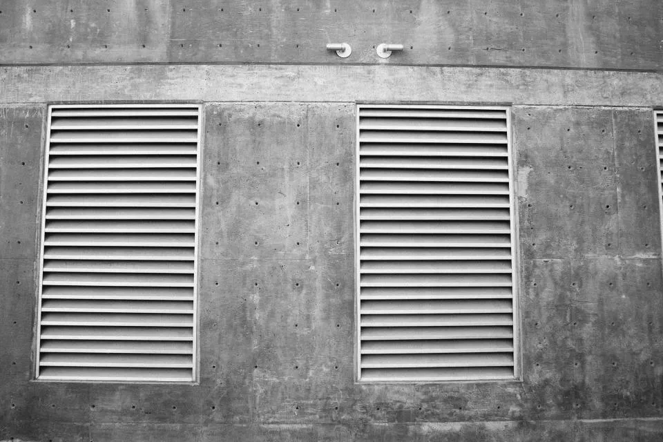 Two louvered air vents in a concrete wall, a reminder that nail salon ventilation moves vapors out of the room